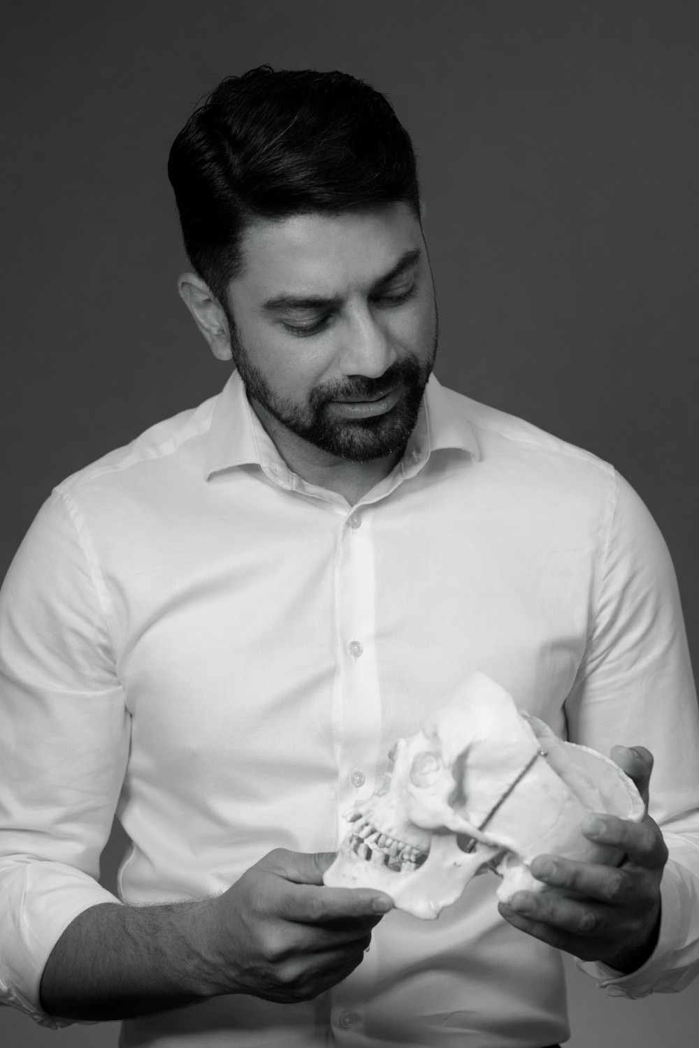 Black and white editorial portrait of Dr. Bhargava studying a skull model
